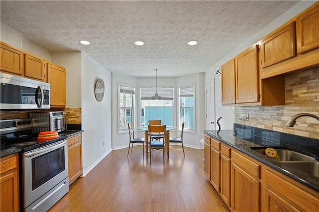 kitchen with wood finished floors, baseboards, a sink, appliances with stainless steel finishes, and tasteful backsplash