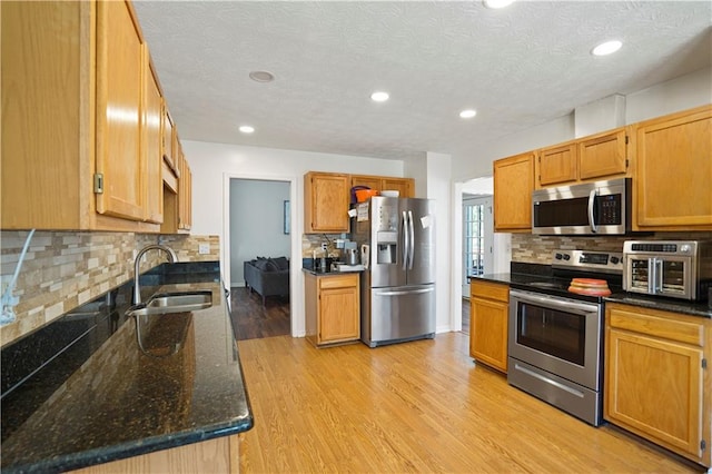 kitchen with light wood-type flooring, a sink, dark stone countertops, stainless steel appliances, and decorative backsplash