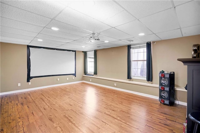 home theater room featuring plenty of natural light, a drop ceiling, baseboards, and wood finished floors