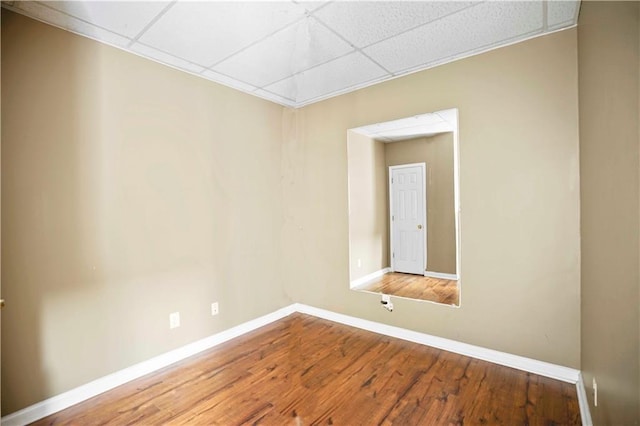 unfurnished room with a paneled ceiling, baseboards, and wood finished floors