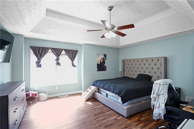 bedroom featuring a tray ceiling, a textured ceiling, wood finished floors, baseboards, and ceiling fan