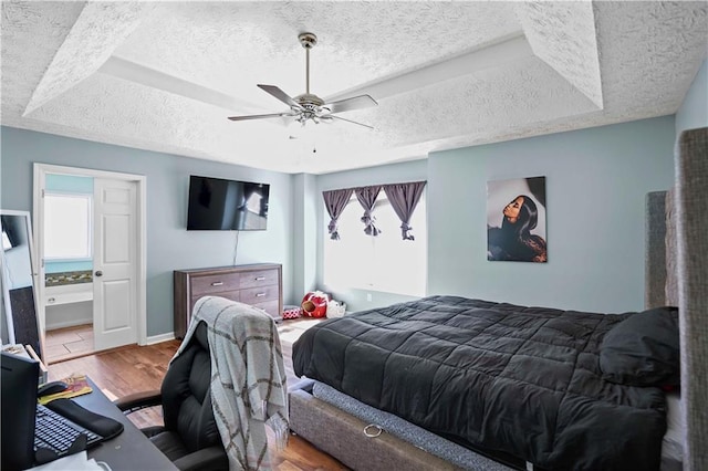 bedroom with baseboards, wood finished floors, a textured ceiling, a raised ceiling, and a ceiling fan