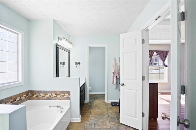 bathroom with a wealth of natural light, a textured ceiling, and a bath