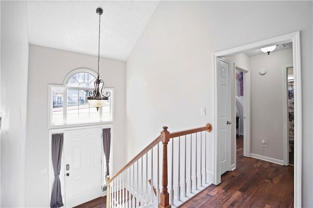 entrance foyer with a textured ceiling, lofted ceiling, an inviting chandelier, and dark wood-style flooring