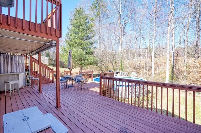 wooden deck with outdoor dining space, fence, and an outdoor pool