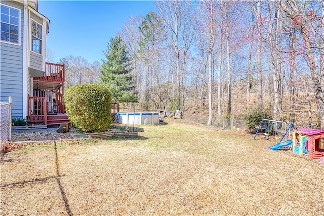 view of yard with a deck, a playground, fence, and an outdoor pool