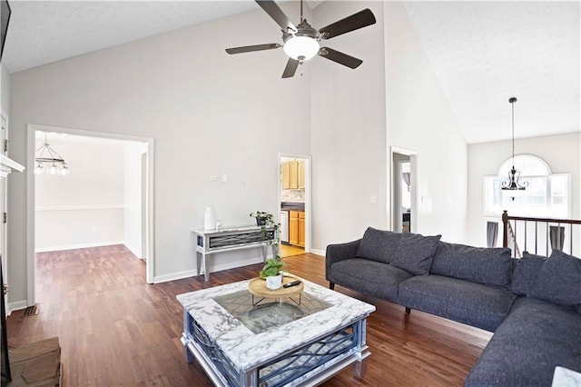 living room with ceiling fan with notable chandelier, dark wood-style floors, baseboards, and high vaulted ceiling