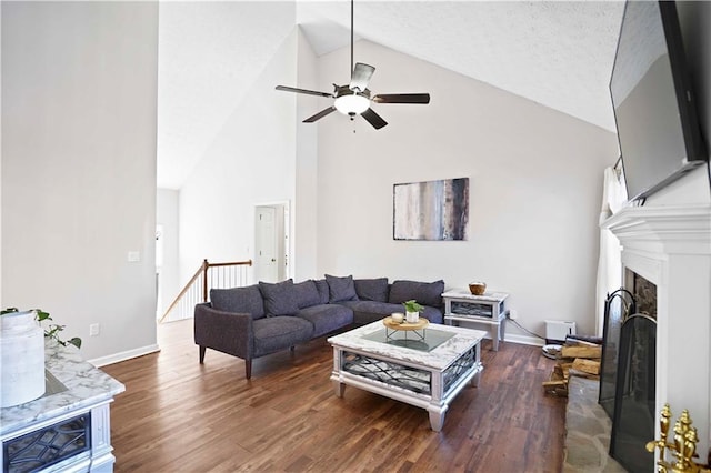 living area with a ceiling fan, wood finished floors, baseboards, high vaulted ceiling, and a fireplace with raised hearth