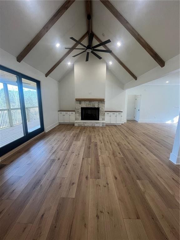 unfurnished living room featuring light wood finished floors, ceiling fan, a fireplace, high vaulted ceiling, and beam ceiling