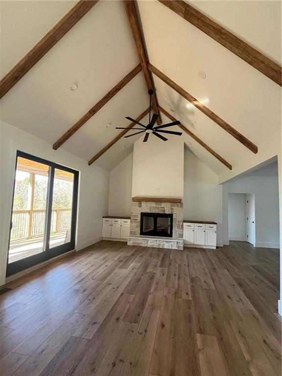 unfurnished living room with high vaulted ceiling, beamed ceiling, a stone fireplace, and wood finished floors