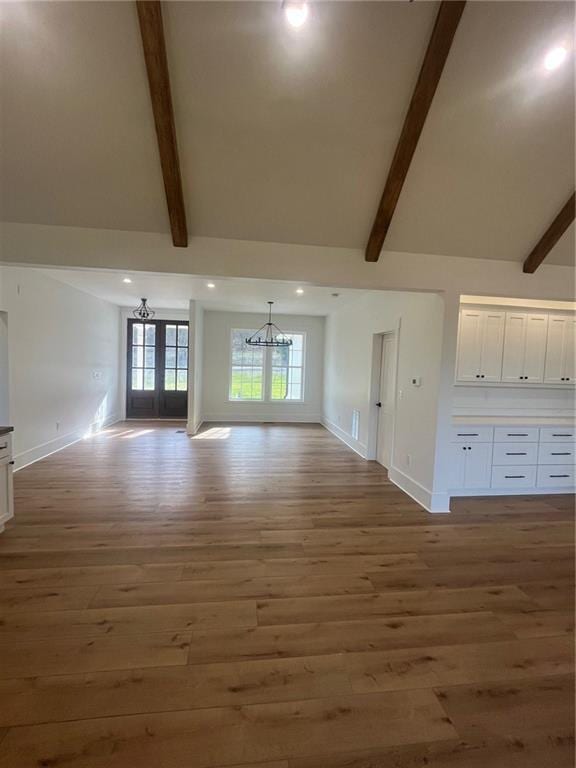 unfurnished living room with dark wood-style flooring, a notable chandelier, and vaulted ceiling with beams