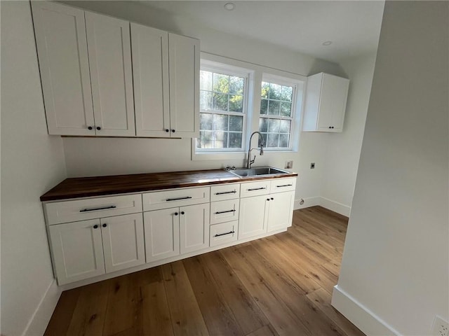 kitchen featuring light wood-type flooring, butcher block counters, white cabinetry, and a sink