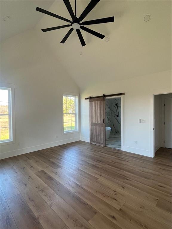 interior space with a barn door, a ceiling fan, wood finished floors, high vaulted ceiling, and baseboards