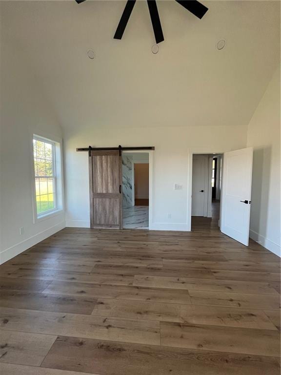 unfurnished bedroom featuring high vaulted ceiling, a barn door, baseboards, and wood finished floors