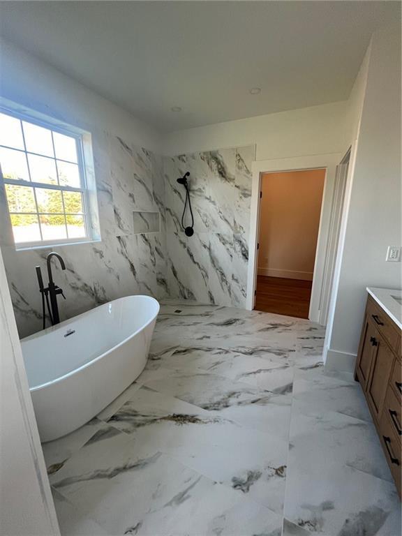 bathroom with marble finish floor, a freestanding tub, and vanity