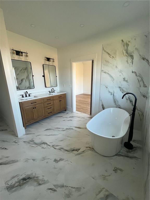 full bathroom with double vanity, marble finish floor, a freestanding tub, and a sink