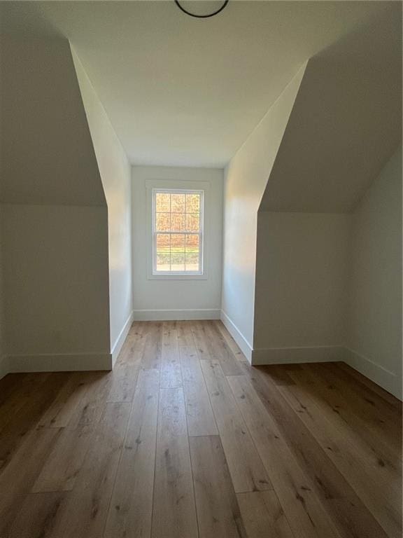 additional living space with light wood-type flooring, baseboards, and vaulted ceiling