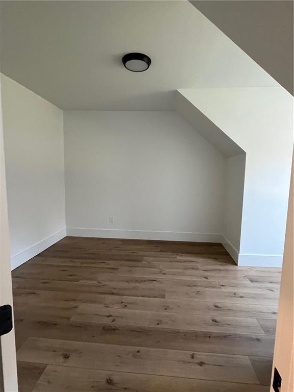 bonus room with baseboards, vaulted ceiling, and wood finished floors