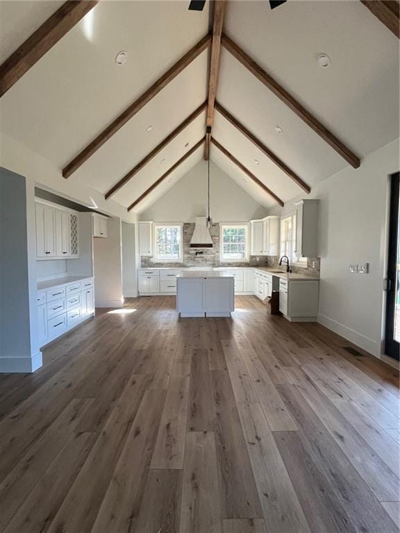 unfurnished living room with a sink, beamed ceiling, wood finished floors, and baseboards