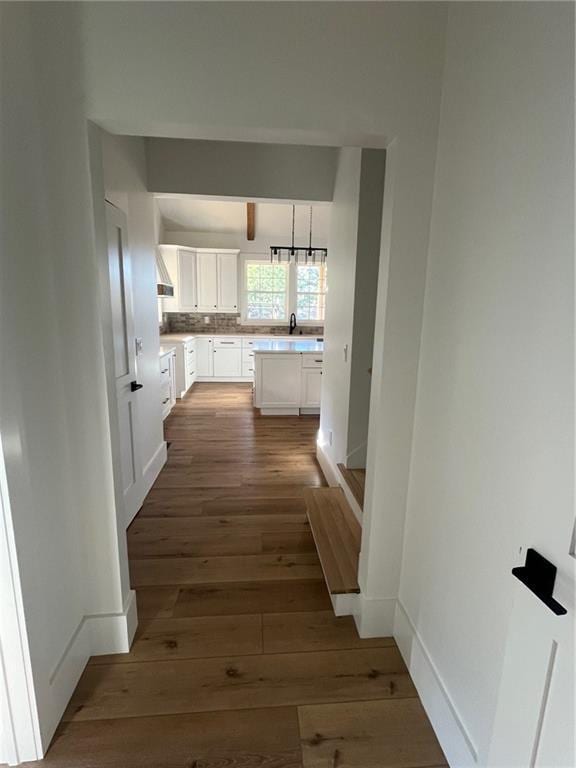 hall featuring dark wood-style flooring, a sink, and baseboards