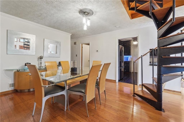 dining space featuring hardwood / wood-style flooring, ornamental molding, and a textured ceiling