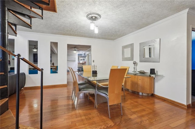 dining space featuring wood-type flooring, a textured ceiling, and crown molding