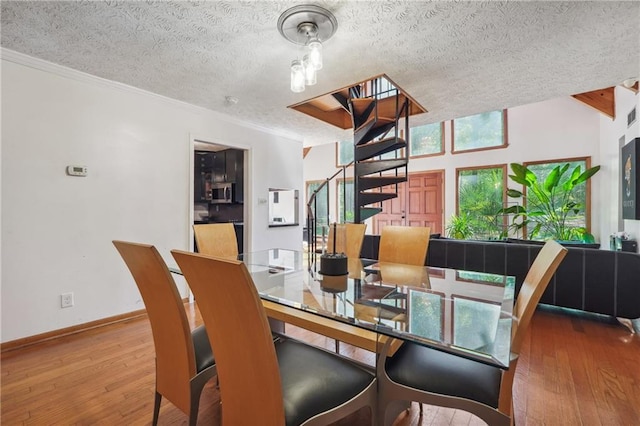 dining space featuring wood-type flooring, a textured ceiling, and ornamental molding