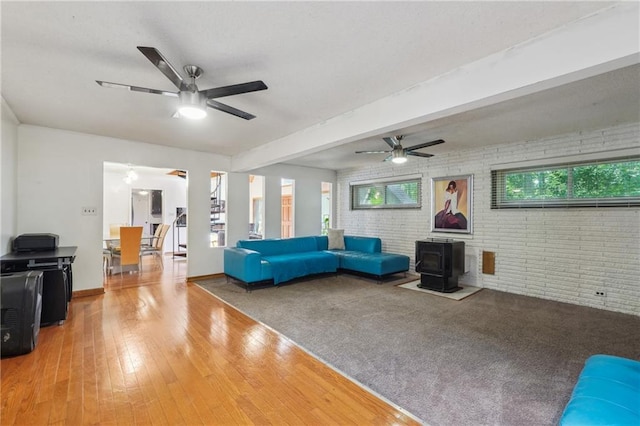 unfurnished living room with a wood stove, ceiling fan, brick wall, and hardwood / wood-style flooring