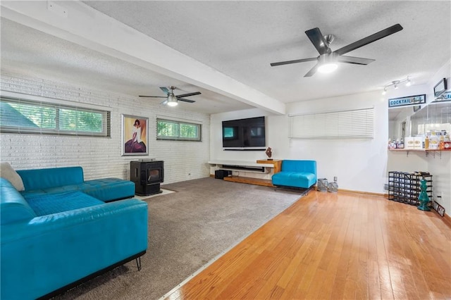 living room featuring brick wall, a wood stove, wood-type flooring, beam ceiling, and ceiling fan