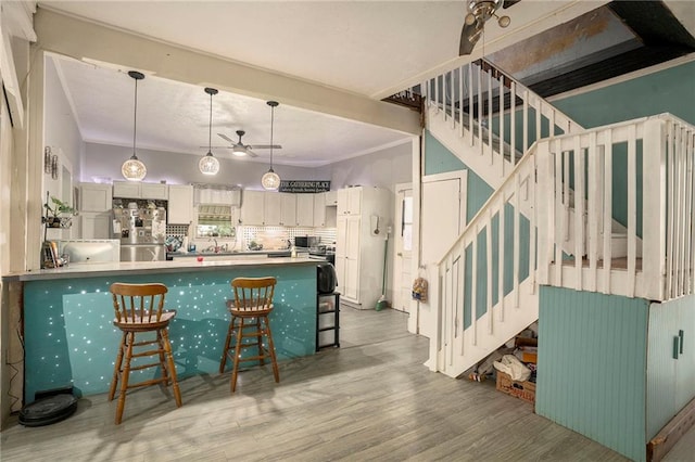 kitchen with white cabinetry, a kitchen bar, backsplash, light wood-type flooring, and stainless steel refrigerator