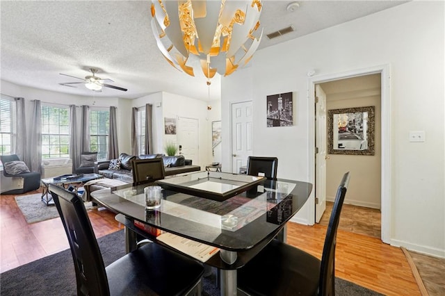 dining area featuring hardwood / wood-style floors, ceiling fan with notable chandelier, and a textured ceiling