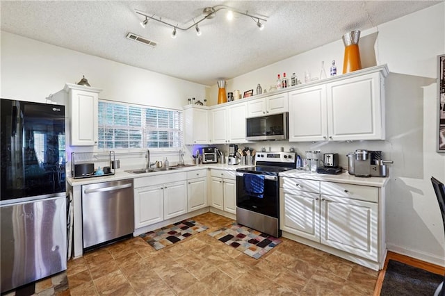 kitchen with white cabinets, appliances with stainless steel finishes, a textured ceiling, and sink