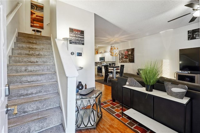 living room featuring wood-type flooring, a textured ceiling, and ceiling fan