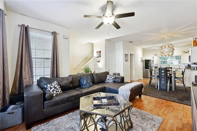 living room featuring ceiling fan with notable chandelier, wood-type flooring, and a textured ceiling