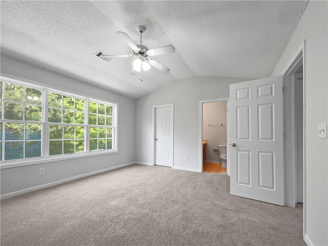 unfurnished bedroom with carpet, vaulted ceiling, ensuite bath, ceiling fan, and a textured ceiling