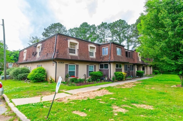 multi unit property featuring mansard roof, stucco siding, and a front yard