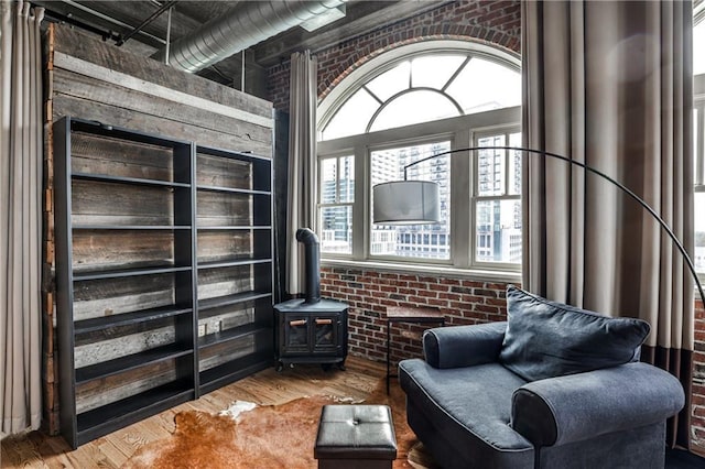 living area with a wood stove, wood finished floors, and brick wall