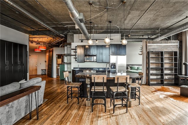 kitchen featuring a kitchen bar, wood-type flooring, appliances with stainless steel finishes, and a towering ceiling