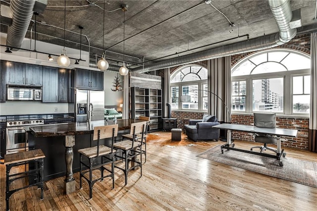 kitchen featuring brick wall, a breakfast bar area, wood finished floors, hanging light fixtures, and stainless steel appliances