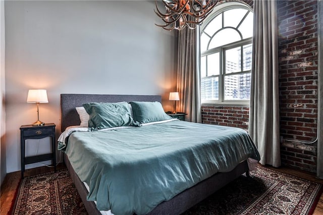 bedroom with dark wood finished floors, a notable chandelier, and brick wall