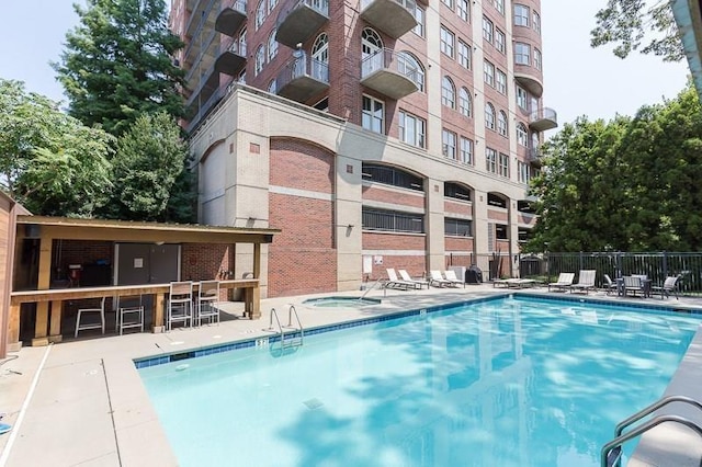 view of swimming pool with a patio, a community hot tub, outdoor dry bar, and fence