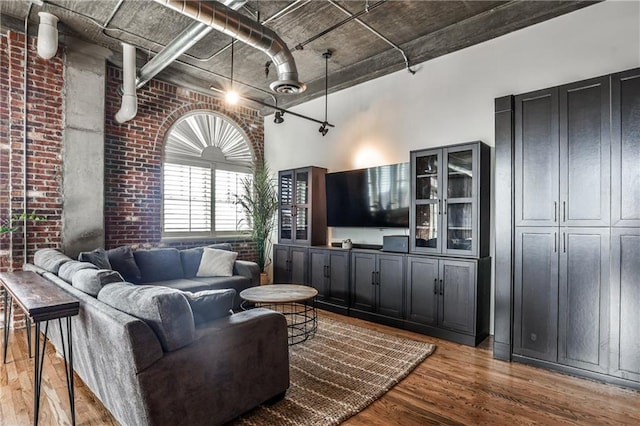 living room featuring brick wall, a high ceiling, and wood finished floors