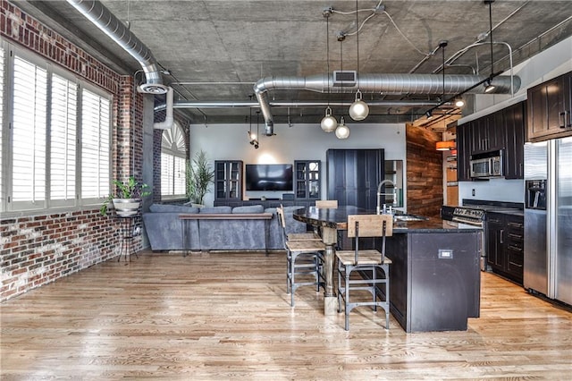 kitchen with brick wall, light wood-style floors, appliances with stainless steel finishes, a towering ceiling, and a kitchen breakfast bar