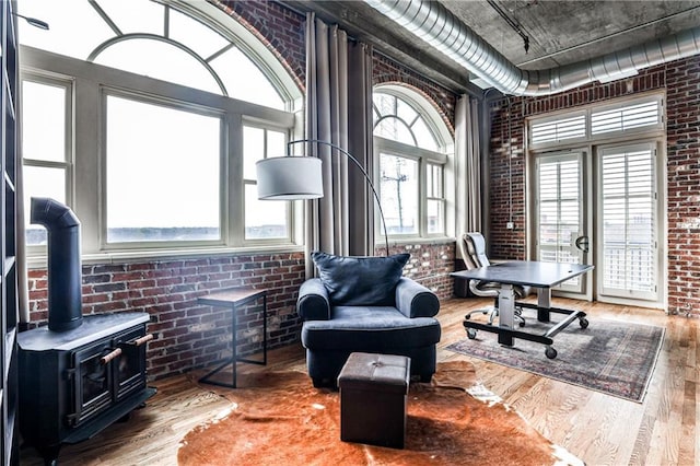 sitting room featuring brick wall, a wood stove, and wood finished floors