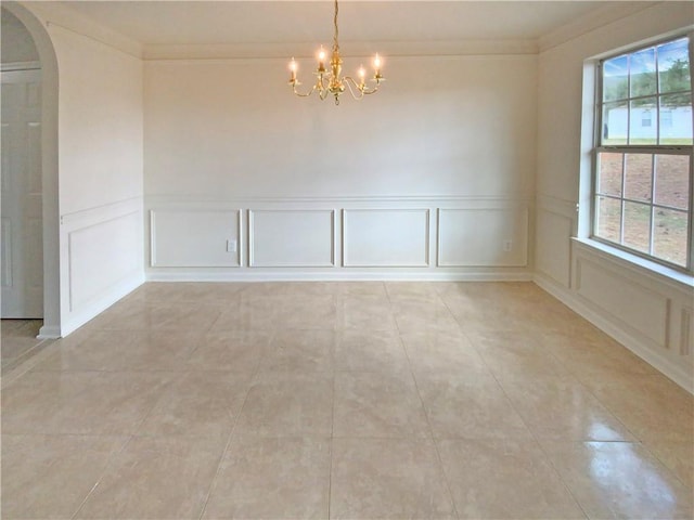 empty room featuring arched walkways, an inviting chandelier, crown molding, a decorative wall, and light tile patterned flooring