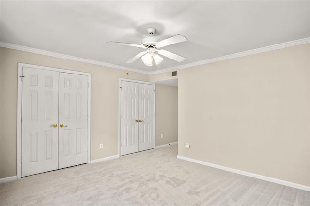 unfurnished bedroom with ceiling fan, light colored carpet, ornamental molding, and two closets