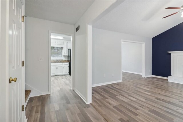 unfurnished living room with a fireplace, ceiling fan, light hardwood / wood-style flooring, and sink