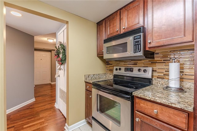 kitchen featuring light hardwood / wood-style floors, light stone countertops, appliances with stainless steel finishes, and tasteful backsplash