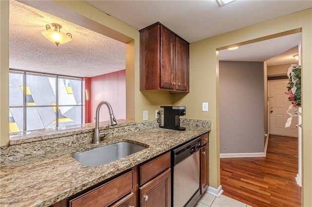 kitchen featuring light stone countertops, sink, light hardwood / wood-style flooring, stainless steel dishwasher, and a textured ceiling