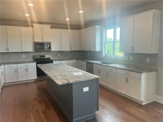 kitchen featuring appliances with stainless steel finishes, dark wood-type flooring, white cabinets, a center island, and sink